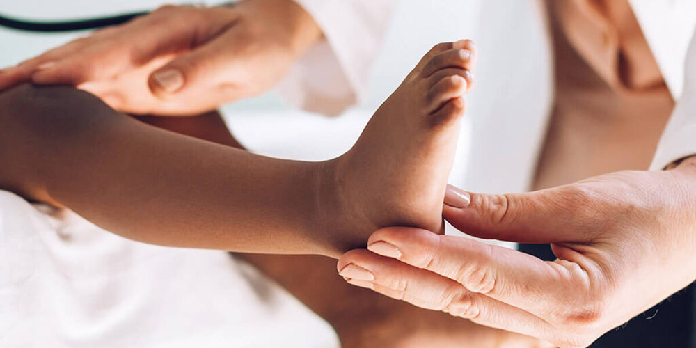 Close-up of a pediatrician examining a child’s leg and foot.