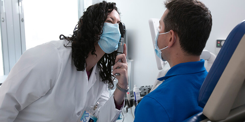 A resident physician who graduated from SGU performs a simple vision exam on a patient sitting in a chair.
