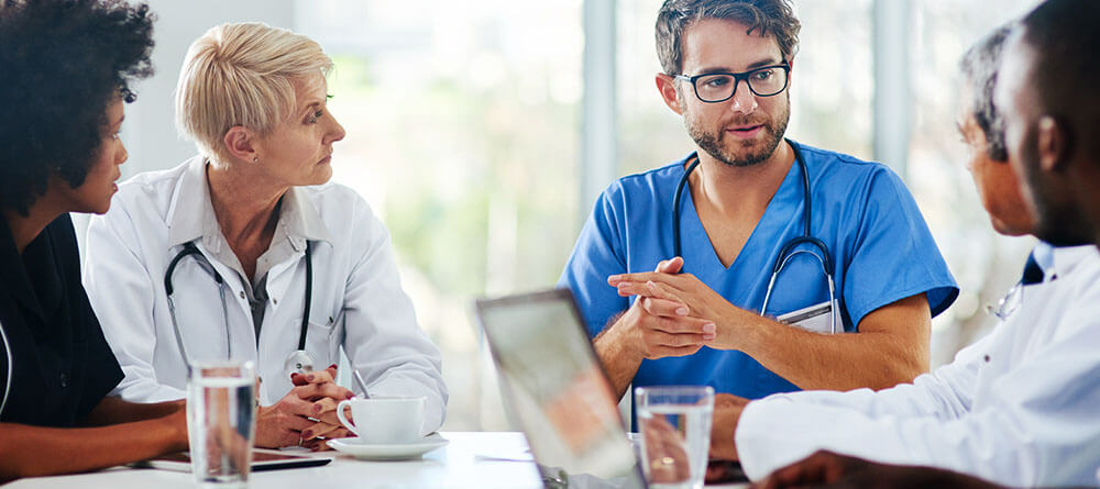 A group of doctors engaged in conversation, sharing ideas and discussing patient care in a bright hospital setting.