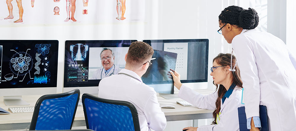 A group of doctors in white lab coats gather around a computer screen, discussing patient data and treatment options.