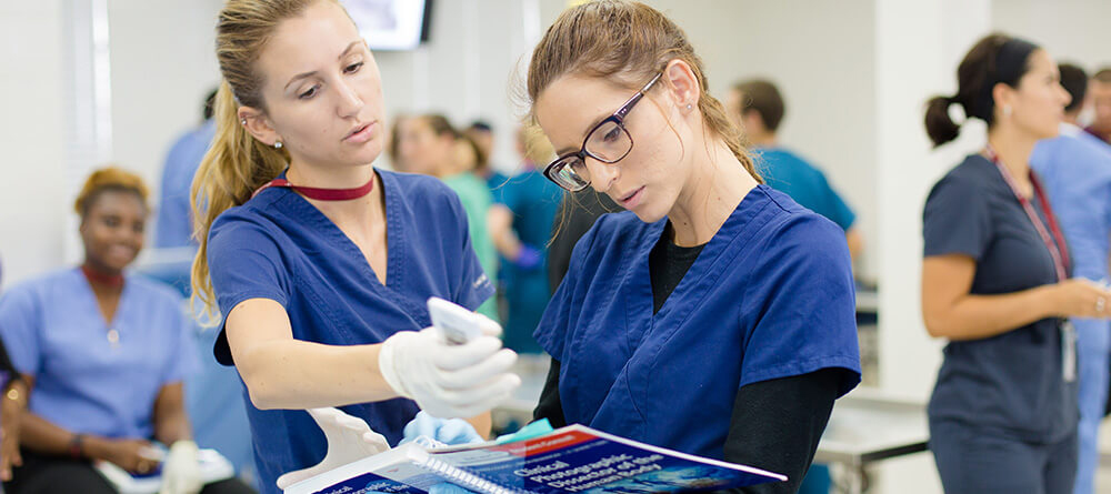 Nurses in blue scrubs smiling while holding a clipboard, ready to assist with patient care and documentation.