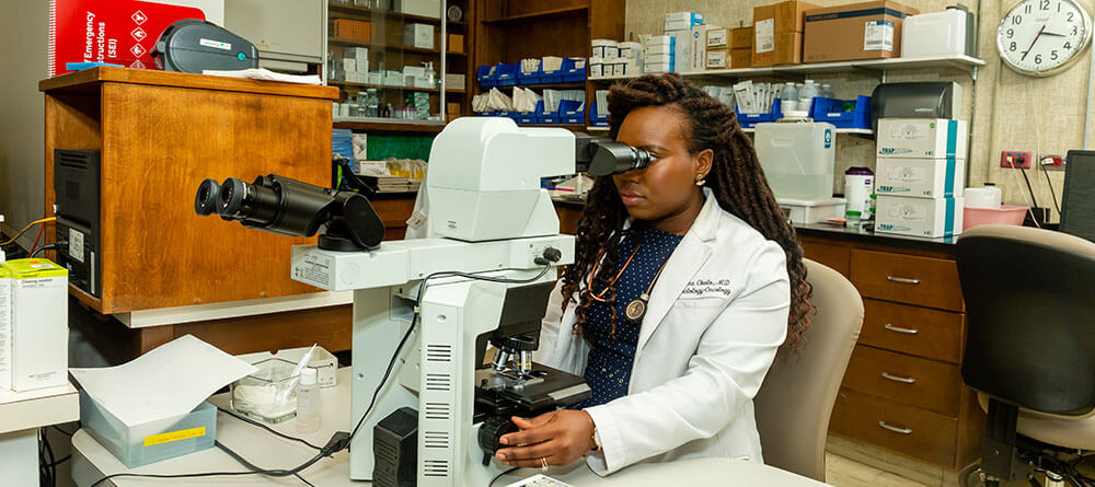 An SGU graduate examines research samples under a microscope