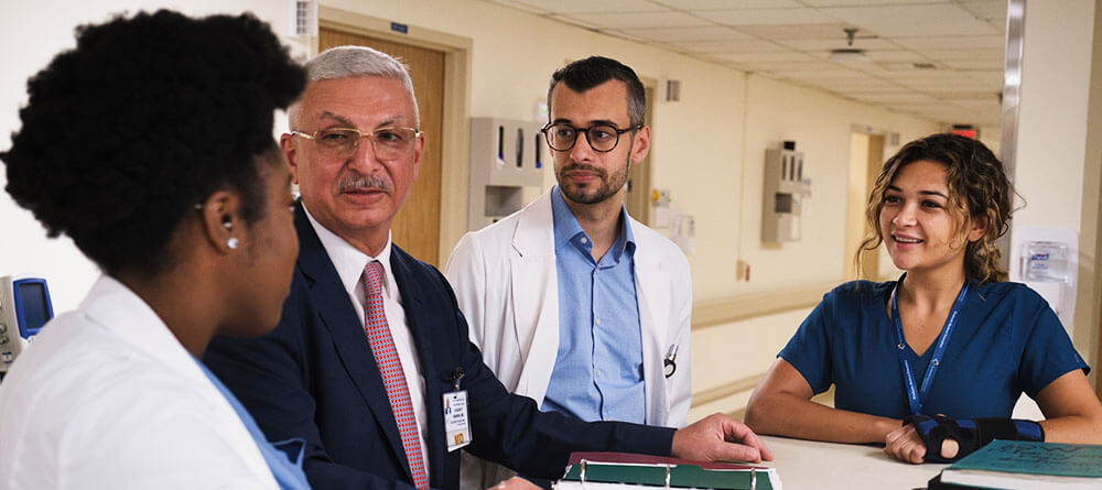 A group of SGU residents converse with a senior doctor at a nurse's station