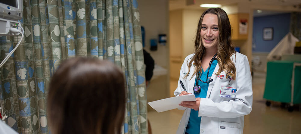 An SGU resident medical student checks on a patient in an ER setting