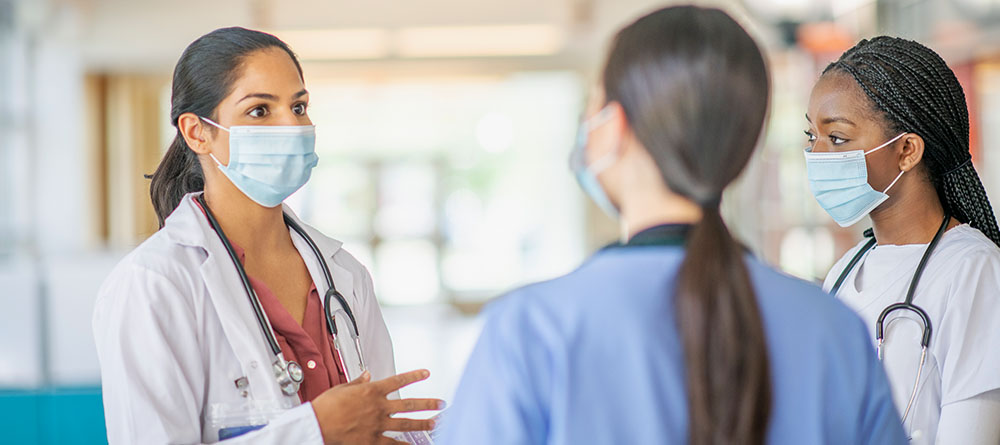 Three women in scrubs having a lively discussion, highlighting collaboration and support in a medical context.