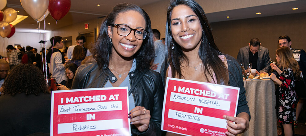 Two SGU medical students holding their residency match cards.