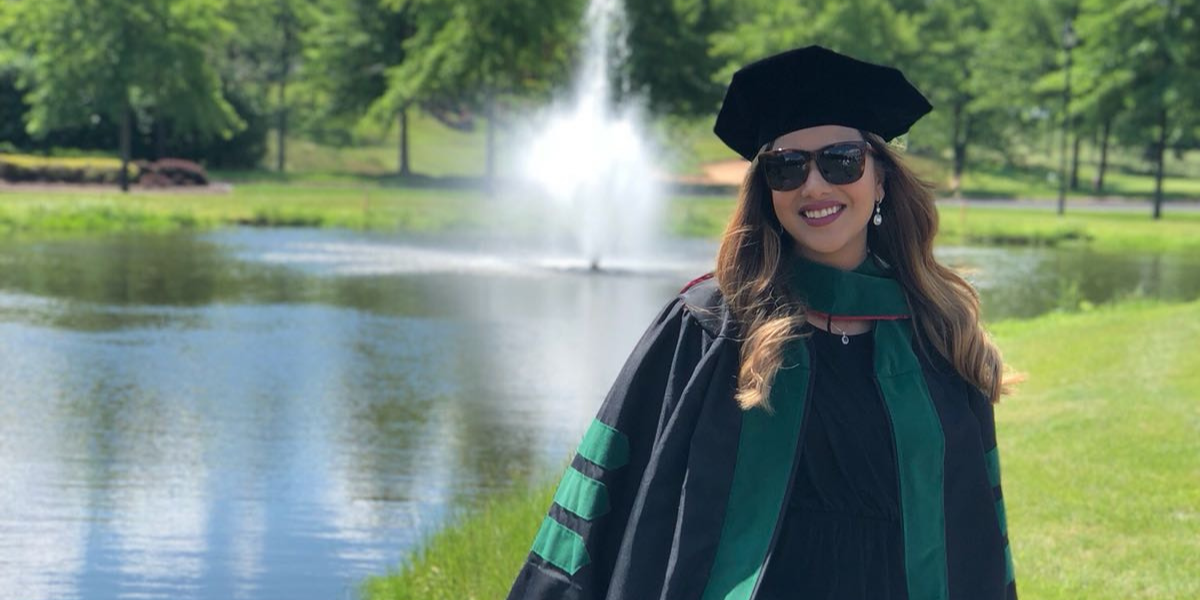 Dr. Mishal Jaleel Akbar in her commencement attire sitting in front of a fountain
