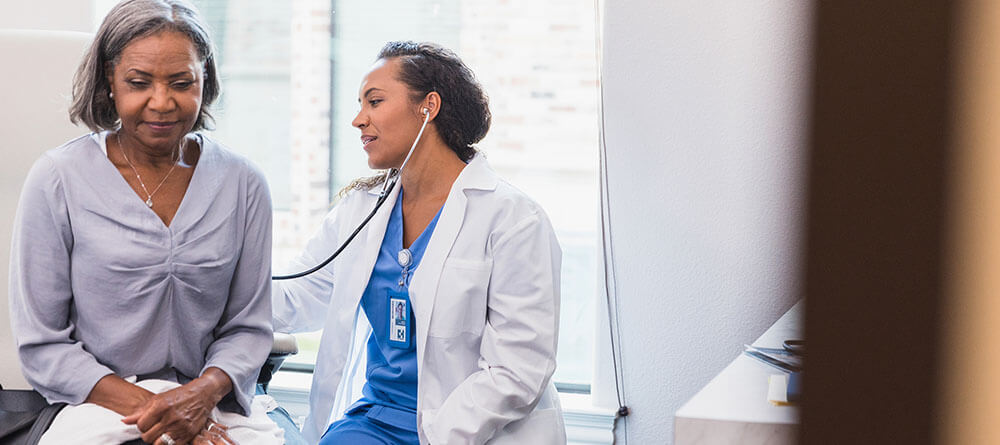 A young family physician performs an exam on an older female patient.