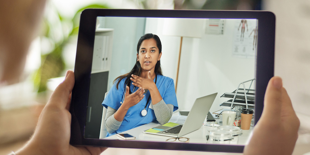 Over the shoulder shot of a patient talking to a doctor using of a digital tablet