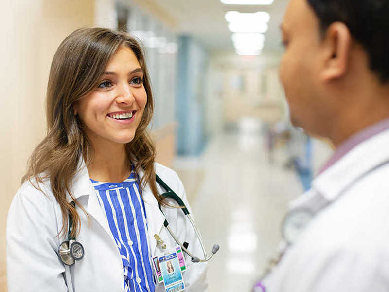 A woman in a white lab coat converses with a man in a white coat.