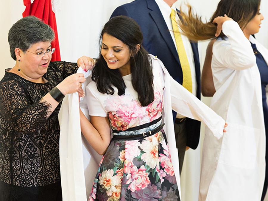 A mother assists a student in putting on a white coat for the ceremony