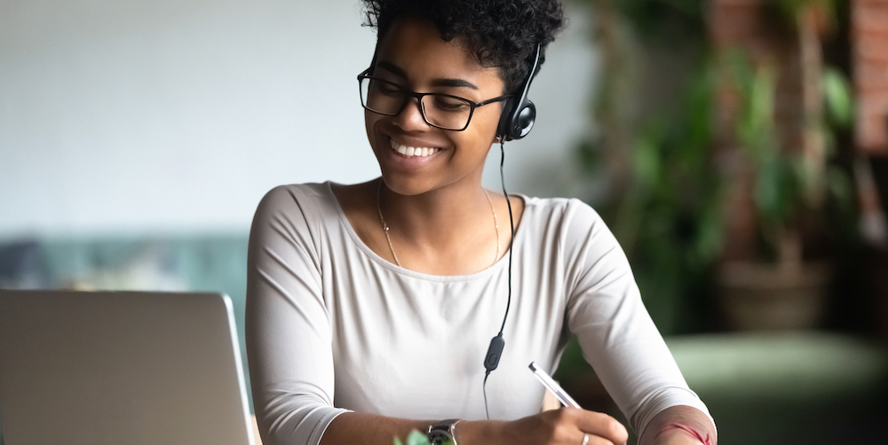 Smiling biracial female in earphones studying making notes