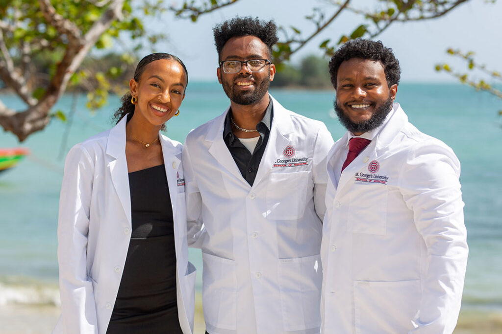 Three SGU students in white coats on the beach